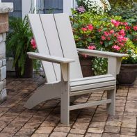 Off-white POLYWOOD Modern Curveback Adirondack Chair situated on a stone paver patio surrounded by blooming garden planters.
