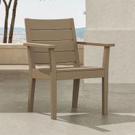 Sand-colored POLYWOOD® Latitude Dining Arm Chair placed on a sunlit stone patio terrace overlooking an open scenic landscape.