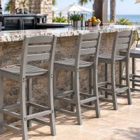 Four grey POLYWOOD La Casa Café bar chairs arranged along an outdoor stone patio bar counter