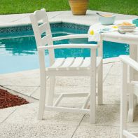 White POLYWOOD La Casa Café patio dining arm chair placed on a paved poolside deck next to a dining table