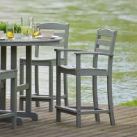 Grey POLYWOOD La Casa Café counter arm chairs placed around an outdoor round table on a lakeside deck